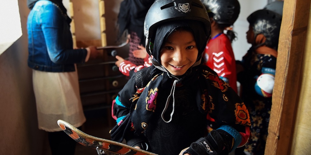 A smiling girl holding her skateboard.